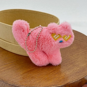 Close-up of pink plush cat charm with heart embroidery and fluffy fur texture detail