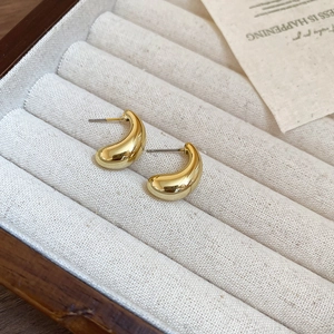 Macro detail of polished gold teardrop earrings resting on a soft beige velvet jewelry box