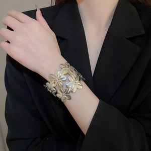 Detailed close-up of a brushed gold metal floral cuff bracelet on a black blazer sleeve