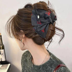 Detail of black fabric bow hair claw clip with red embroidery worn by a model