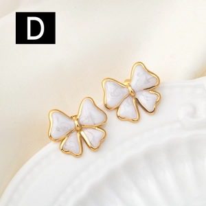 Detailed close-up of golden bow-shaped stud earrings with white marble texture enamel