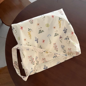 Close-up of floral print on beige canvas tote bag with a woven brand tag on a wood table