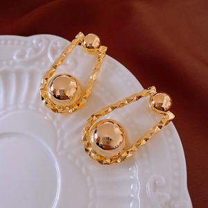 Detail view of gold sphere earrings with a wavy frame on a velvet and ceramic background