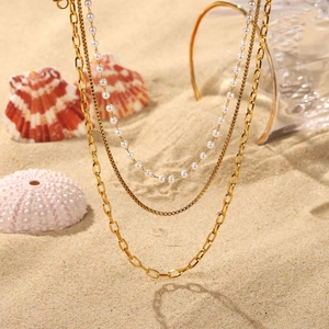 Three-layer gold necklace with pearls and link chains on a summery beach background