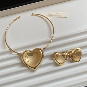 Detail of golden heart pendant necklace and stud earrings set on a white textured tray