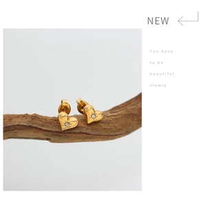 Close-up of golden heart earrings with zircon center inlay on a wooden display