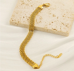 Detail of gold woven mesh bracelet with lobster clasp on a beige stone and silk background