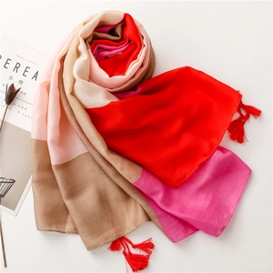 Detail of color-block scarf with red fringe tassels on a soft beige background