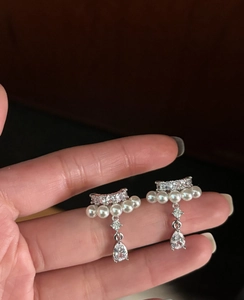 Detailed view of silver drop earrings featuring white pearls and waterdrop zircon held by hand