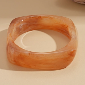Close-up of wide square amber resin bangle with marbled orange and brown textures