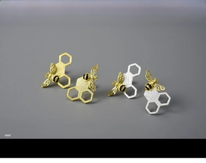 Detailed close-up of asymmetrical sterling silver honeycomb and golden bee stud earrings
