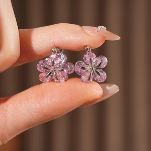 Gros plan de boucles d'oreilles fleurs en zircon rose et métal argenté tenues à la main