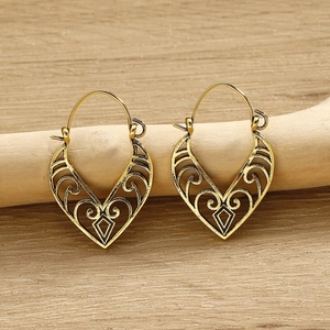 Detailed close-up of golden bohemian earrings with hollow heart motifs on wooden stand