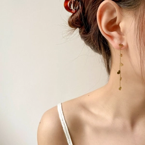 Close-up of golden heart-shaped long tassel drop earrings worn by a model in soft light