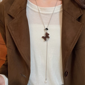 Detail of a flocked horse pendant necklace with pearl charm on a stylish model outfit