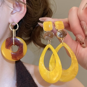 Macro detail of large resin drop earrings featuring tortoiseshell textures and yellow hues