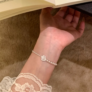 Detailed view of rose flower charm and pearl bracelet on a model's wrist