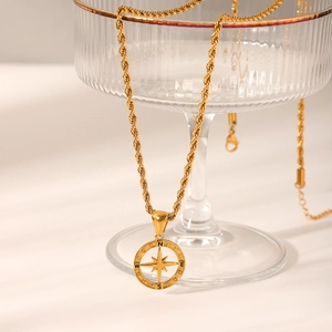 Collana con ciondolo a bussola dorata con catena a corda appesa a un bicchiere