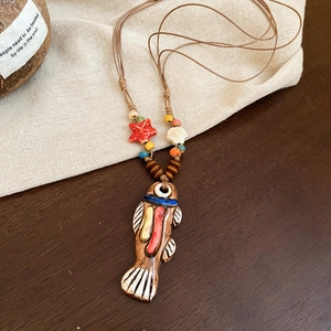 Close-up of ceramic fish pendant and starfish beads on a braided ethnic style necklace