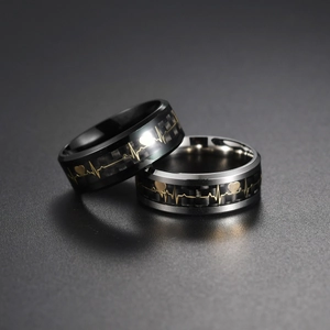 Macro detail of 8mm carbon fiber rings with gold EKG heartbeat pattern and heart symbol