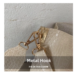 Detailansicht goldener Metallhaken und beigem Kroko-Prägeleder an der modischen Schultertasche