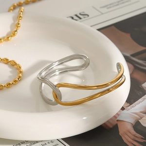 Detail of two-tone twisted open cuff bracelet in gold and silver finish on a ceramic tray
