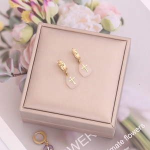Boucles d'oreilles créoles dorées avec pierre rose et breloque croix sur boîte à bijoux