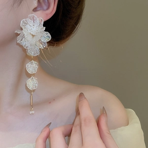 Detail of white acrylic flower tassel earrings worn by a model showing elegant drape