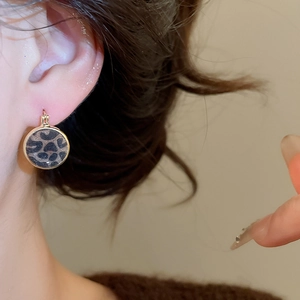 Macro shot of a model wearing leopard print round earrings with golden metal borders