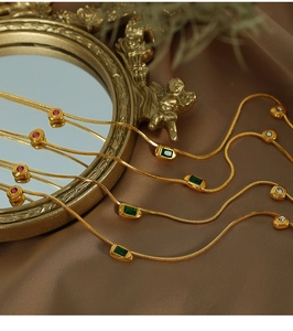 Detail of vintage gold snake chains with emerald and ruby gemstone pendants on dark fabric