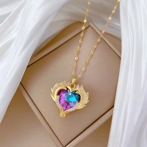 Luxurious gold heart necklace with colorful gemstone and diamond wings on silk fabric