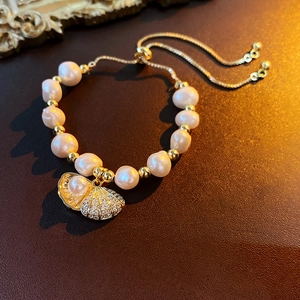 Macro shot of freshwater pearl bracelet with gold shell pendant on leather background