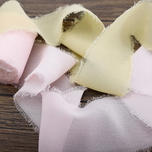 Frayed edge chiffon ribbons in pink and pale yellow on a dark wood texture background