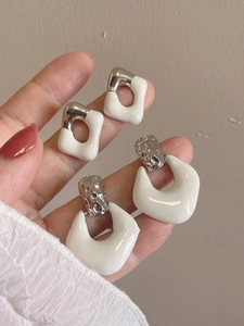 Detail of cream enamel geometric square and round earrings held for size reference