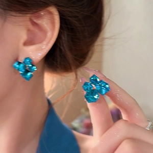 Macro detail of geometric blue crystal stud earrings worn by a model in soft lighting