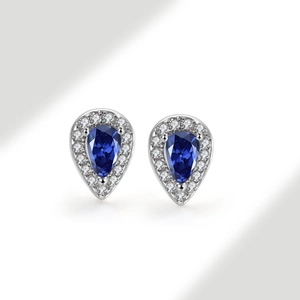 Macro shot of silver teardrop stud earrings featuring a blue pear-shaped center stone