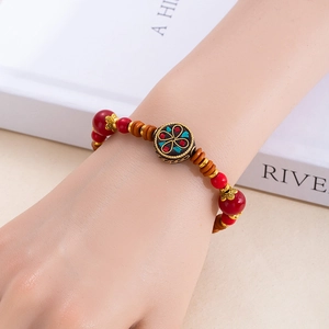 Gros plan d'un bracelet ethnique perlé avec perles rouges et charme émaillé sur le poignet
