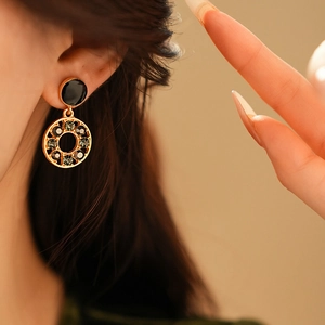 Gros plan d'un mannequin portant une boucle d'oreille dorée en émail noir et gemmes sombres