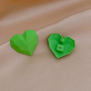 Detail of matte green geometric heart stud earrings with silver pins on silk background