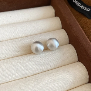 Macro detail of silver brushed round stud earring with textured matte metallic finish