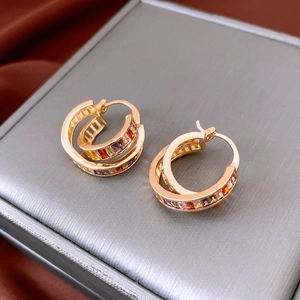 Macro shot of gold double-hoop earrings with colorful square zircons on silk background