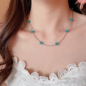 Dettaglio di una collana argentata con perle blu occhio di gatto indossata da modella