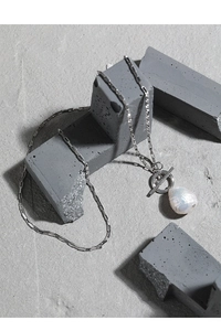 Detail of baroque pearl pendant with silver T-bar toggle clasp on textured stone