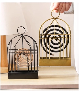 Detail of birdcage iron mosquito coil holder in black and gold finishes on a wooden desk