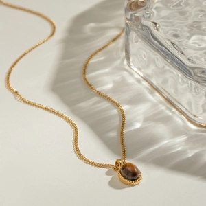18k gold plated stainless steel necklace with oval tiger eye stone pendant on a flat surface