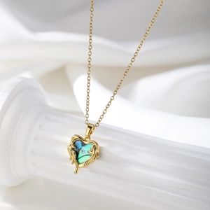 Detail of heart-shaped ocean style gold necklace with iridescent shell inlay on white silk