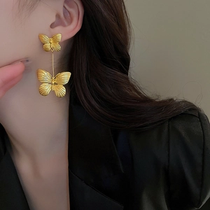 Detail of elegant gold double butterfly long drop earrings worn by a model in close-up