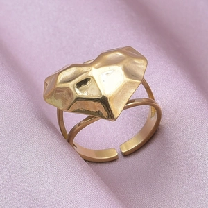 Macro shot of geometric heart-shaped golden ring on pink satin fabric background