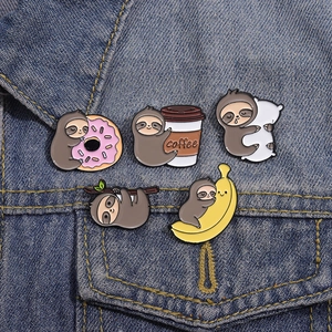 Set of five cartoon sloth enamel pins with donuts and bananas on blue denim fabric