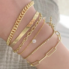 Close-up of layered gold bracelet set featuring Cuban link, snake chain and zircon charms
